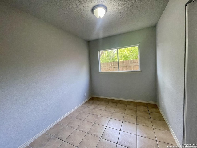 spare room with a textured ceiling, baseboards, and light tile patterned floors