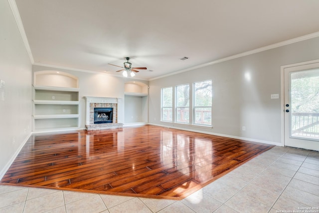 unfurnished living room with built in shelves, crown molding, light tile patterned floors, ceiling fan, and a fireplace