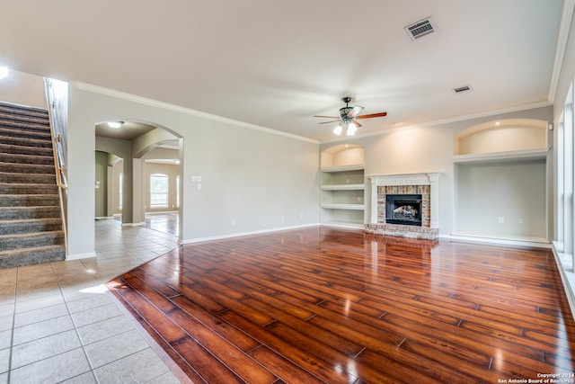 unfurnished living room featuring a brick fireplace, built in features, hardwood / wood-style floors, and ceiling fan