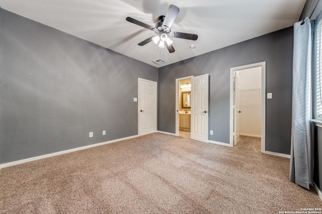 unfurnished bedroom with ensuite bathroom, a walk in closet, carpet flooring, a closet, and ceiling fan