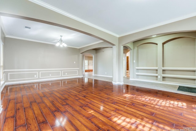 spare room featuring an inviting chandelier, built in shelves, ornamental molding, and hardwood / wood-style flooring