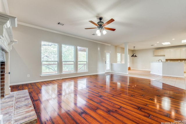 unfurnished living room with sink, a brick fireplace, light wood-type flooring, ornamental molding, and ceiling fan