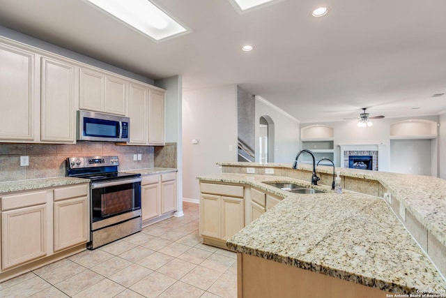 kitchen with light stone counters, stainless steel appliances, sink, and a center island with sink