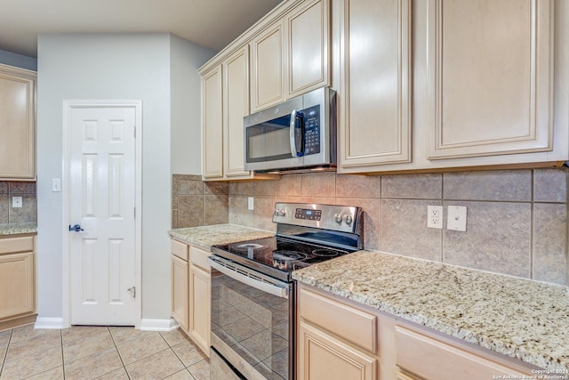 kitchen with tasteful backsplash, light tile patterned floors, stainless steel appliances, light stone countertops, and cream cabinetry