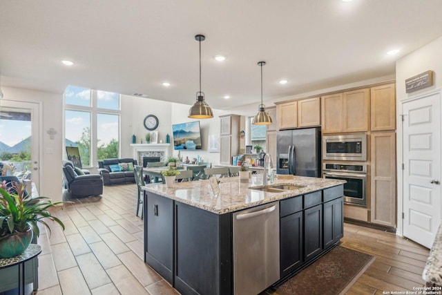 kitchen featuring light brown cabinetry, decorative light fixtures, an island with sink, sink, and stainless steel appliances