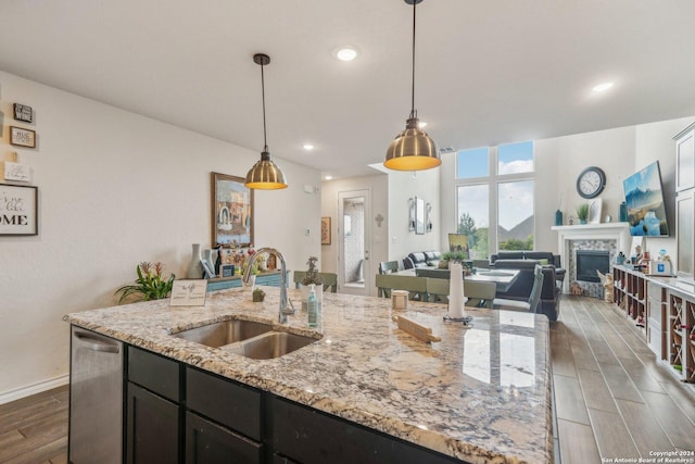 kitchen featuring pendant lighting, sink, a kitchen island with sink, light stone counters, and stainless steel dishwasher