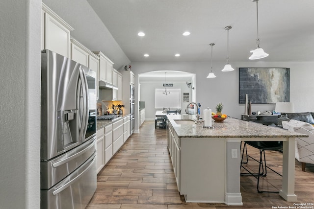 kitchen with sink, stainless steel appliances, white cabinets, a center island with sink, and decorative light fixtures