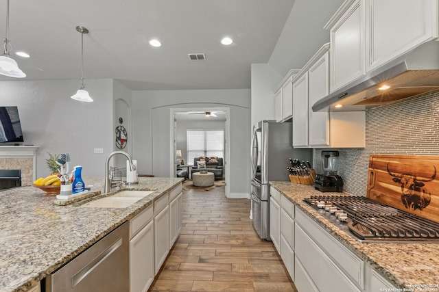 kitchen with sink, light stone counters, decorative light fixtures, a tiled fireplace, and white cabinets