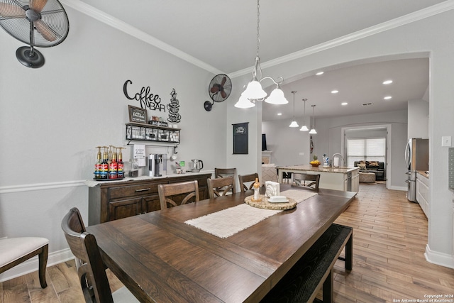 dining room with ornamental molding, sink, and light wood-type flooring