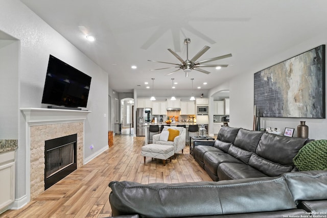 living room featuring a tiled fireplace, ceiling fan, and light hardwood / wood-style floors