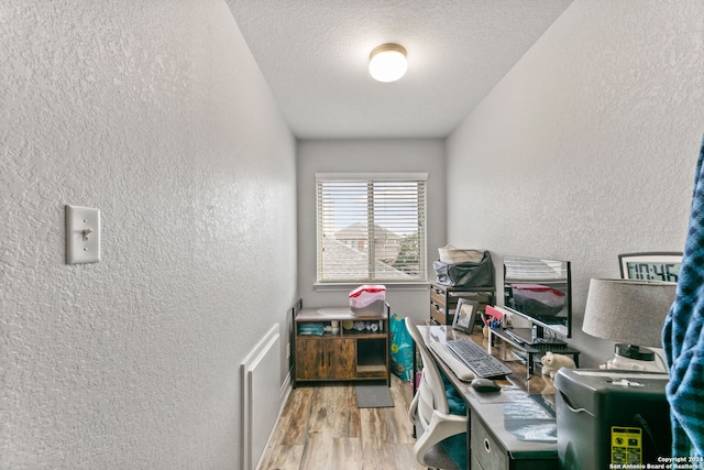 home office with light hardwood / wood-style floors and a textured ceiling