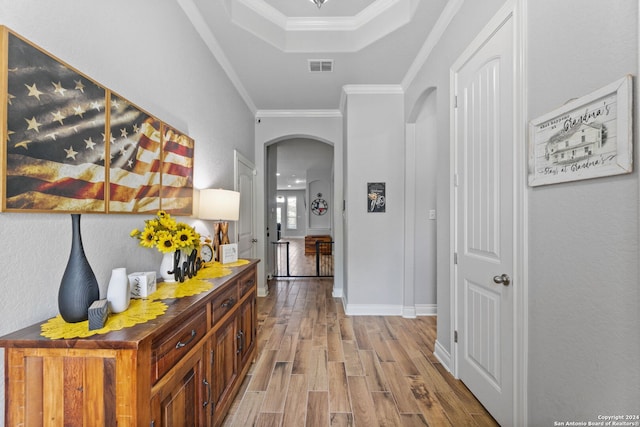 hallway featuring a tray ceiling, light hardwood / wood-style flooring, and ornamental molding