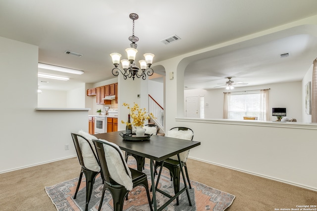 carpeted dining space featuring ceiling fan with notable chandelier