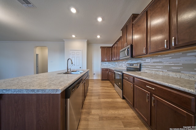 kitchen with appliances with stainless steel finishes, sink, light hardwood / wood-style floors, decorative backsplash, and an island with sink