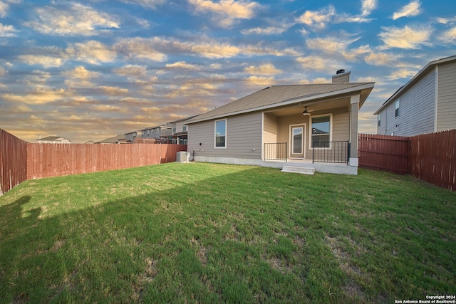 back house at dusk with a patio, cooling unit, a yard, and ceiling fan