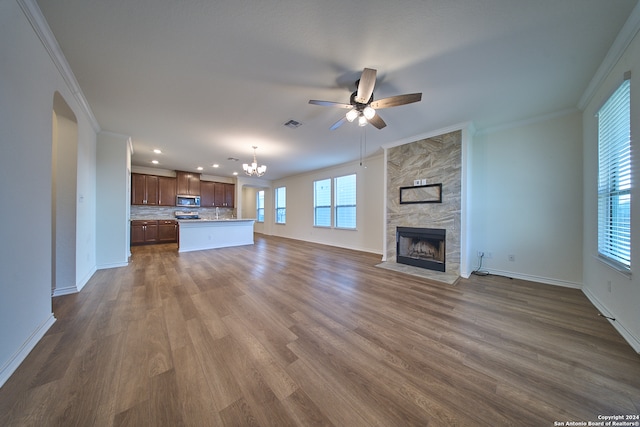 unfurnished living room with hardwood / wood-style flooring, ceiling fan with notable chandelier, ornamental molding, and a large fireplace