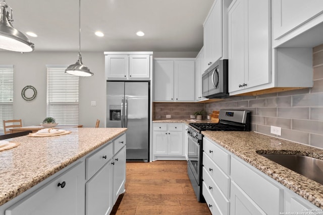 kitchen with stainless steel appliances, white cabinetry, light wood-style floors, light stone countertops, and decorative light fixtures