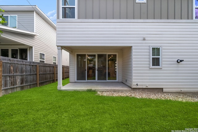 rear view of property with board and batten siding, a patio, a lawn, and fence