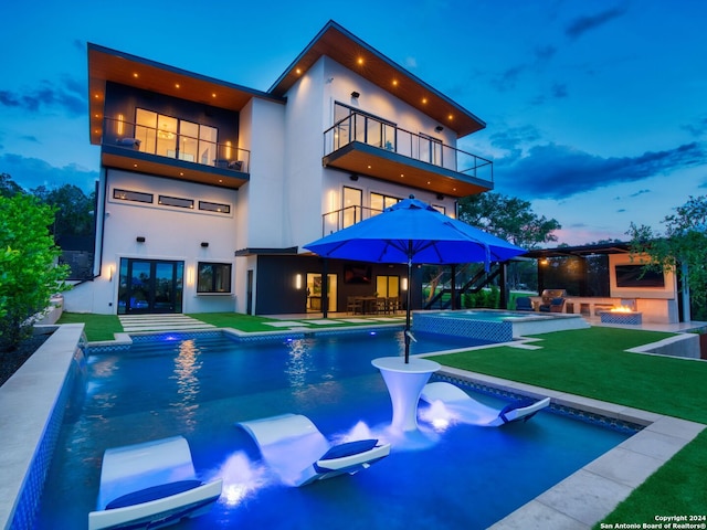 back house at dusk featuring a balcony, a yard, and a patio area