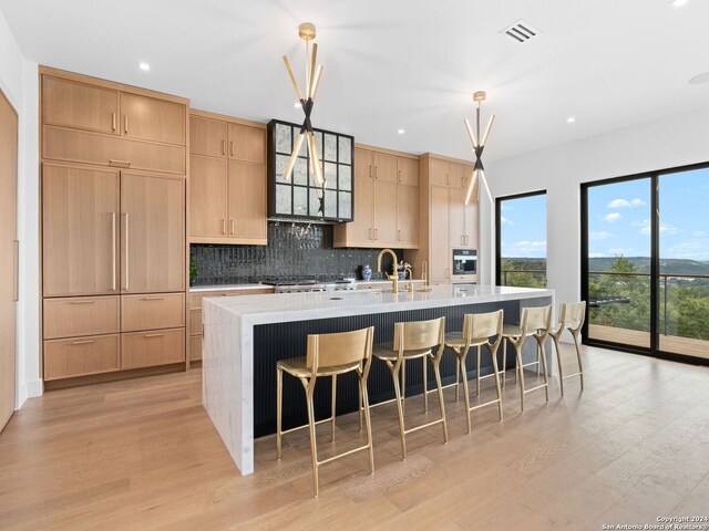 kitchen with decorative light fixtures, tasteful backsplash, light wood-type flooring, an island with sink, and stove