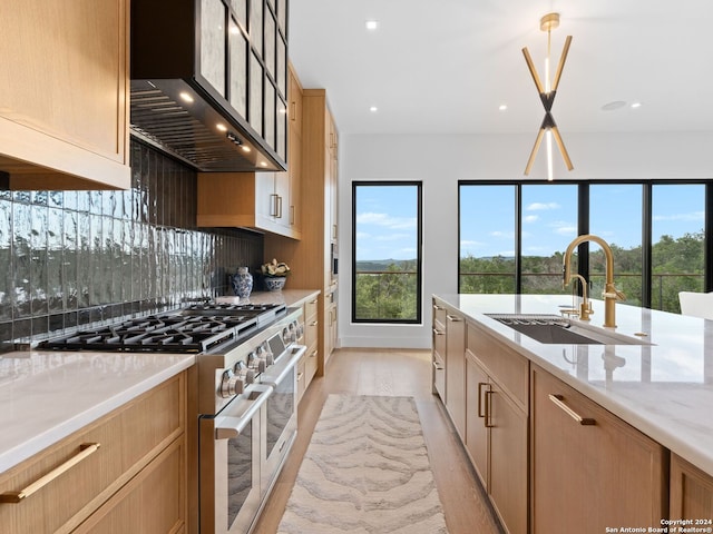 kitchen with a sink, wall chimney range hood, light stone countertops, stainless steel range, and decorative light fixtures