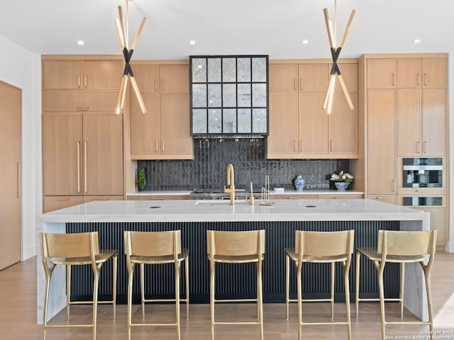 kitchen featuring wood-type flooring, light brown cabinetry, decorative backsplash, sink, and a center island with sink