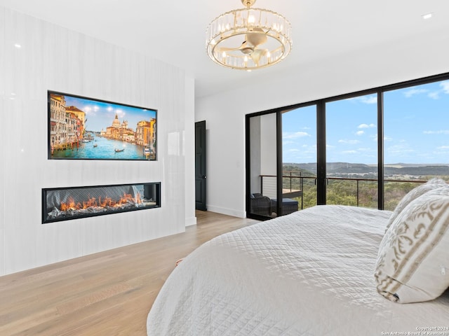 bedroom featuring light wood-type flooring, a glass covered fireplace, access to exterior, and a notable chandelier