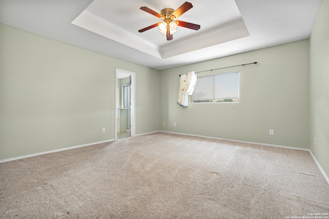 carpeted spare room with a tray ceiling, crown molding, and ceiling fan