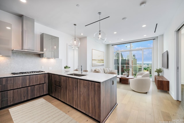 kitchen featuring light wood-type flooring, wall chimney range hood, backsplash, stainless steel gas cooktop, and expansive windows