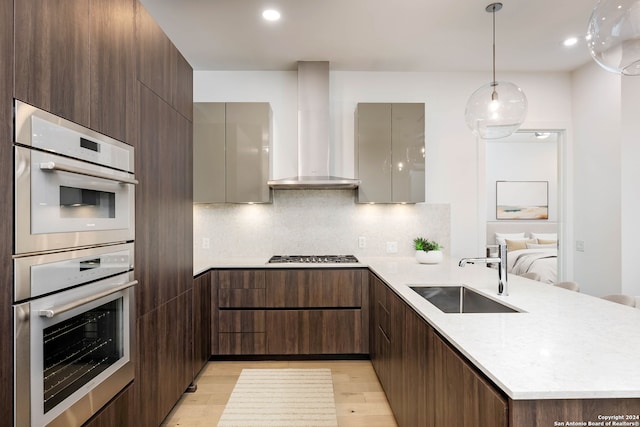 kitchen with double wall oven, light wood-type flooring, wall chimney range hood, backsplash, and sink