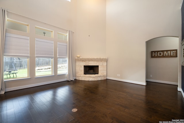 unfurnished living room with a fireplace, a high ceiling, and dark wood-type flooring