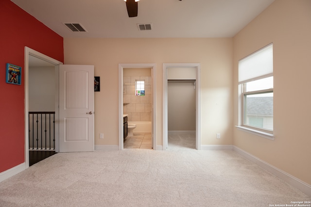 unfurnished bedroom with light carpet, multiple windows, ensuite bath, and a walk in closet