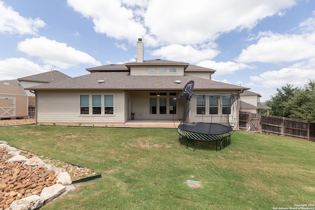 rear view of property with a trampoline, a storage unit, a patio, and a yard