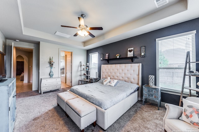 bedroom with carpet flooring, connected bathroom, ceiling fan, and a tray ceiling