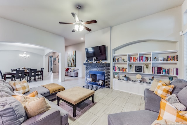 living room featuring ceiling fan with notable chandelier, built in shelves, a brick fireplace, and light tile patterned floors