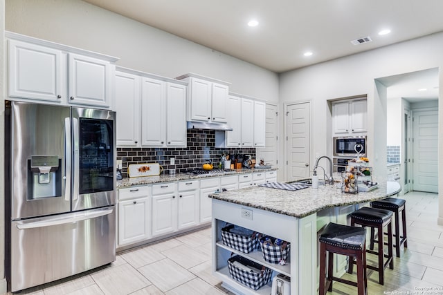 kitchen featuring light stone counters, stainless steel appliances, backsplash, and white cabinets