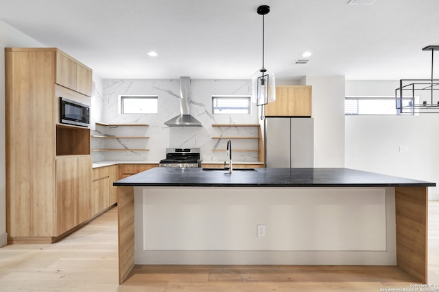 kitchen with stainless steel appliances, sink, a kitchen island with sink, and wall chimney range hood