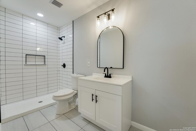 bathroom featuring tiled shower, vanity, tile patterned flooring, and toilet