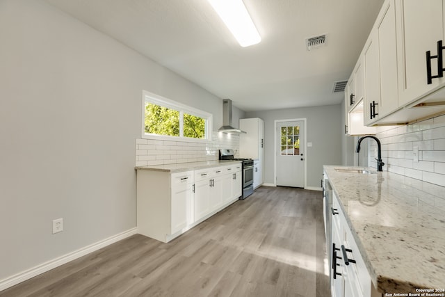 kitchen with stainless steel gas range oven, light wood-type flooring, wall chimney range hood, decorative backsplash, and sink