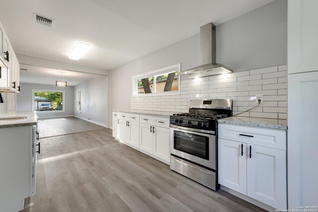 kitchen with range with two ovens, light wood-type flooring, white cabinets, and wall chimney range hood