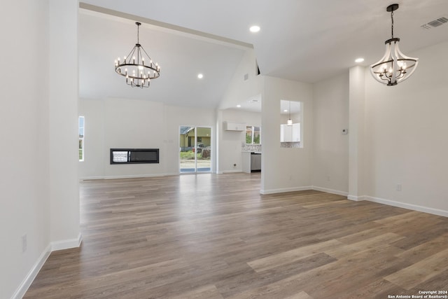 unfurnished living room featuring hardwood / wood-style flooring, vaulted ceiling, and an inviting chandelier