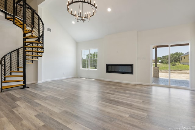 unfurnished living room featuring high vaulted ceiling, light hardwood / wood-style floors, and a chandelier