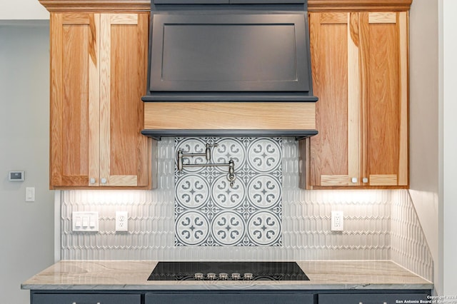 kitchen featuring light stone countertops, black electric stovetop, and backsplash