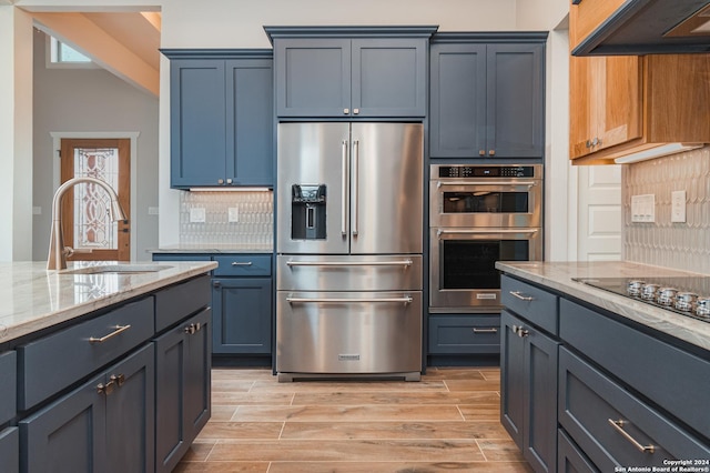 kitchen with sink, exhaust hood, light stone counters, stainless steel appliances, and backsplash