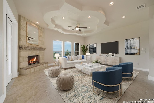 tiled living room with a tray ceiling, a fireplace, and ceiling fan