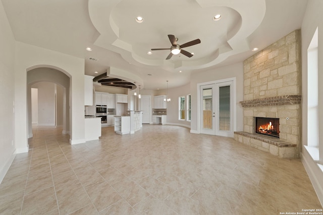 unfurnished living room featuring ceiling fan, light tile patterned floors, a fireplace, and a tray ceiling