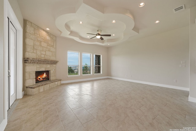 unfurnished living room with a raised ceiling, ceiling fan, light tile patterned flooring, and a fireplace