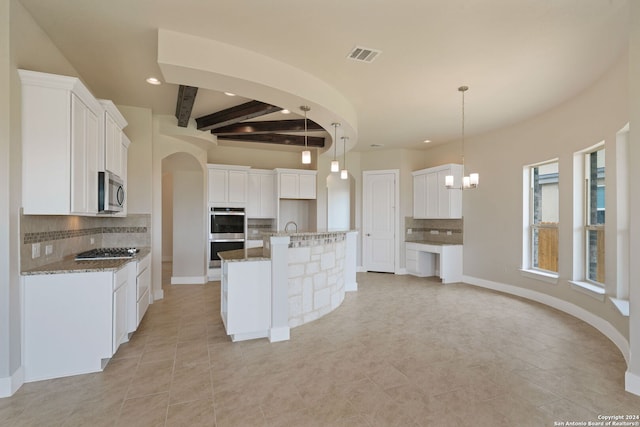 kitchen featuring appliances with stainless steel finishes, hanging light fixtures, an island with sink, white cabinets, and stone countertops