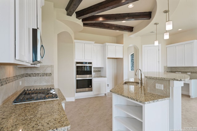 kitchen featuring white cabinetry, sink, hanging light fixtures, stainless steel appliances, and a center island with sink