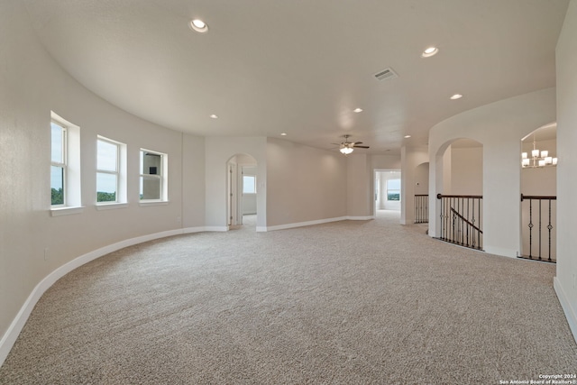 carpeted spare room featuring ceiling fan with notable chandelier